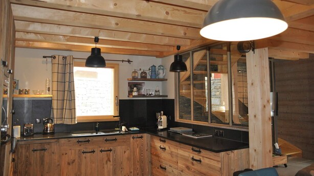 A wooden cabin interior with a kitchen area, wooden beams on the ceiling, and a large window. - Cosy Valloire Family Chalet (Valloire)