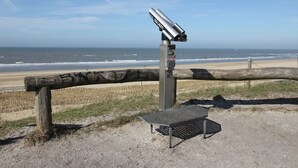 A beach with a wooden fence, a metal bench, and a security camera. - Holiday Home Egmond Near Dune Beaches (Egmond-Binnen)