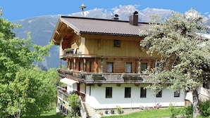 Ein mehrstöckiges Holzhaus mit Balkonen, einer Treppe und Blick auf die Berge im Hintergrund.
