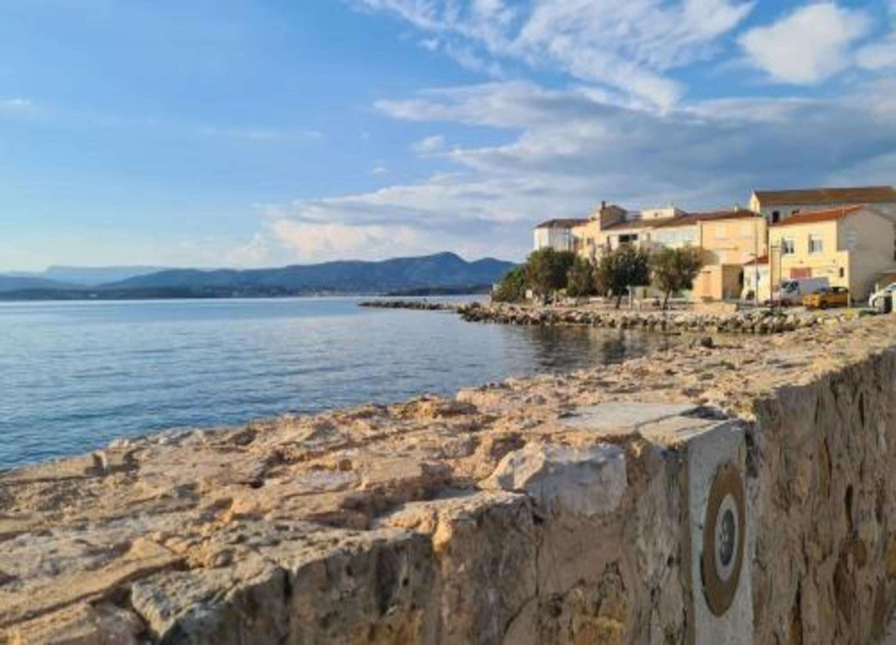 A coastal building with a rocky shoreline, a clear view of the sea, and distant mountains.