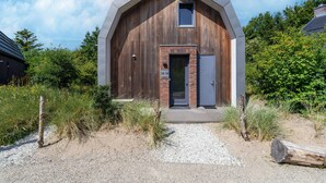 A modern barn-style building with a wooden exterior, a small window, and a door with a number plate. - Holiday Home Waterland for six Person (Egmond aan den Hoef)