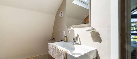 A modern bathroom with a skylight, a large mirror, and a towel hanging on the wall.