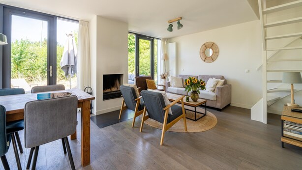 A modern living room with a fireplace, a sofa, a dining table, and a staircase. - Holiday Home Waterland for six Person (Egmond aan den Hoef)