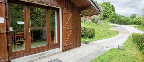 Un edificio in legno con ampie porte in vetro, un ingresso pavimentato e un sentiero che conduce a una strada.