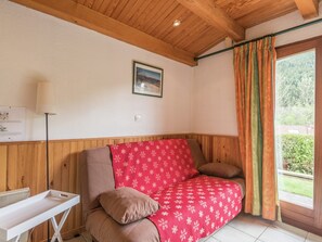 Een gezellige kamer met een houten plafond, een witte radiator, een rode sofa met patroon en een raam met gordijnen.