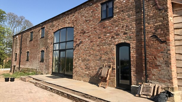 A brick building with large windows and a small outdoor area with steps and a wooden chair. - Luxury Stunning 5 Bed Barn Conversion Near Chester (Chester)
