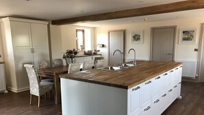 A modern kitchen with a wooden island, white cabinetry, and a dining area with patterned chairs. - Luxury Stunning 5 Bed Barn Conversion Near Chester (Chester)