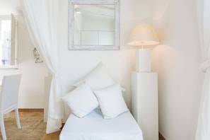 Um quarto branco com uma cama, um abajur, um espelho e uma cadeira.