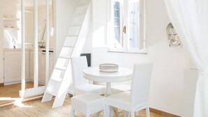 A white room with a round table, chairs, a ladder, and a window with curtains.