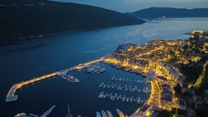 An aerial view of a marina with boats docked, a waterfront promenade, and buildings along the shore.