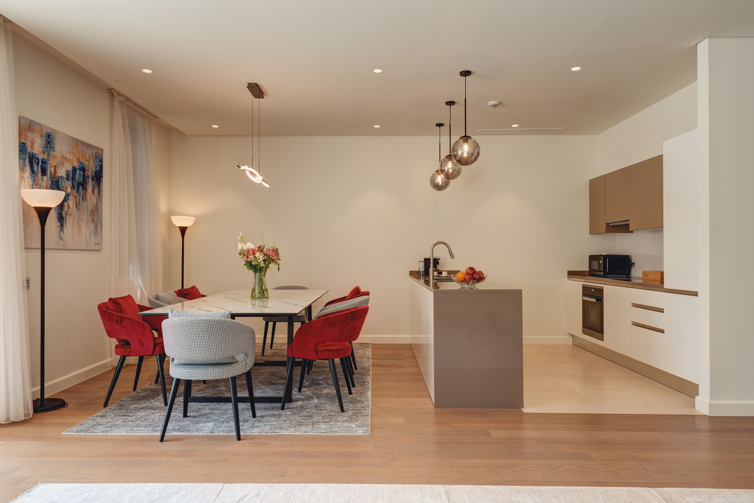 Una cocina moderna con una isla central, un comedor con sillas rojas y un cuadro en la pared.
