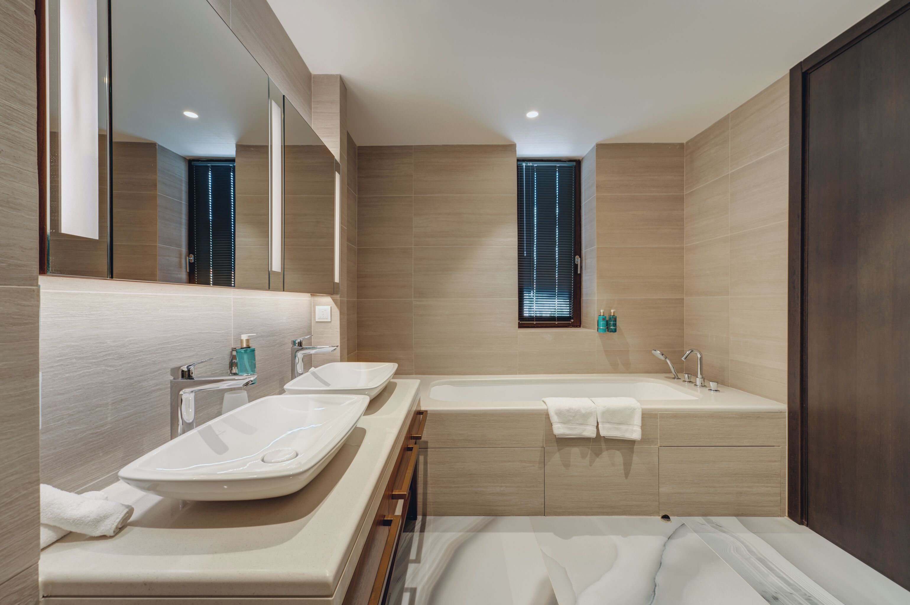A modern bathroom with two sinks, a bathtub, and a large mirror.