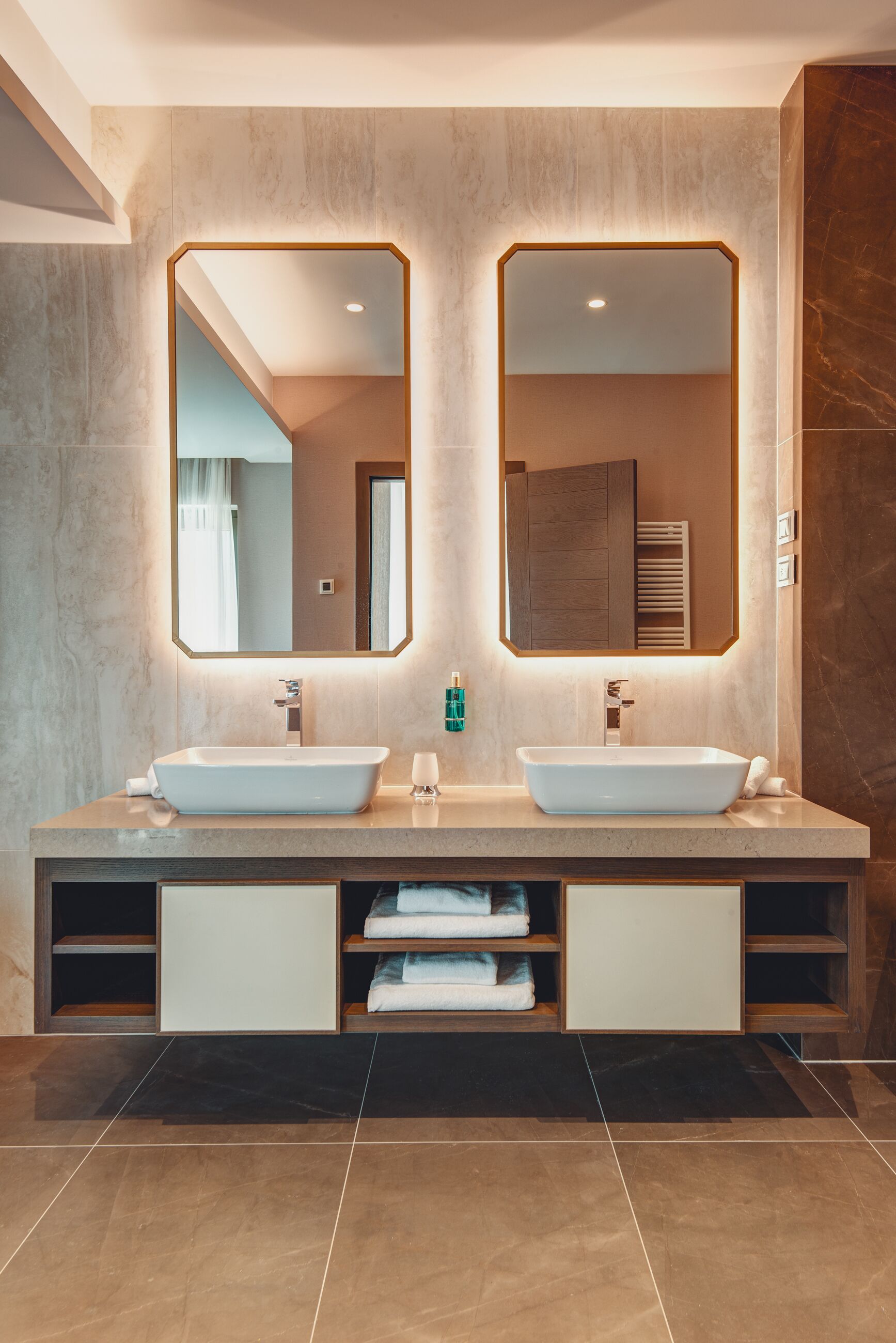 A modern bathroom with two sinks, a large mirror, and a built-in towel rack.
