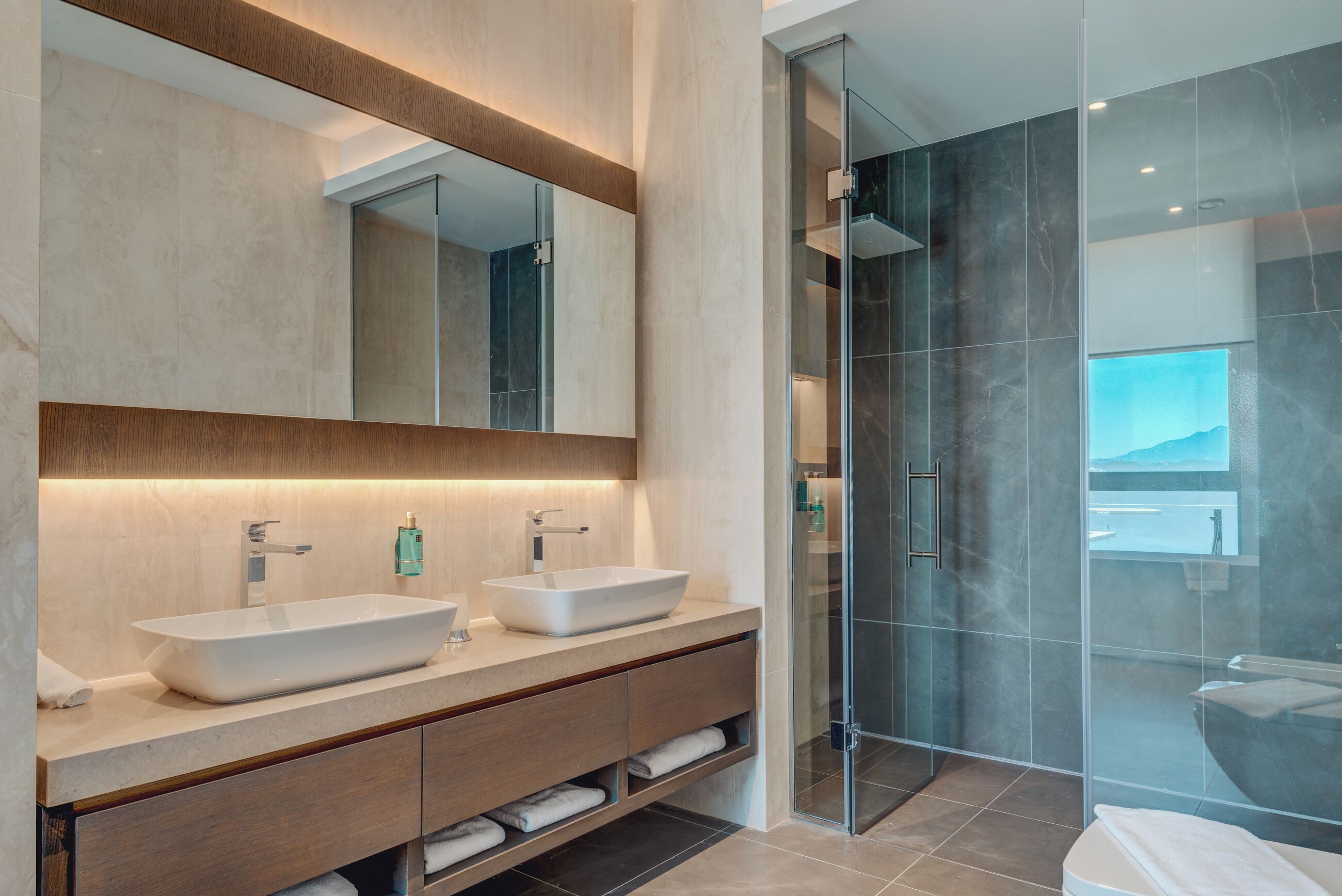 A modern bathroom with two sinks, a large mirror, and a glass shower enclosure.