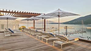 A wooden deck with lounge chairs and umbrellas overlooking a marina and mountains.