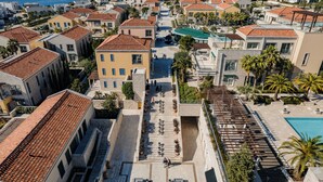 A coastal residential area with terracotta-roofed buildings, a central courtyard with steps, and a swimming pool.