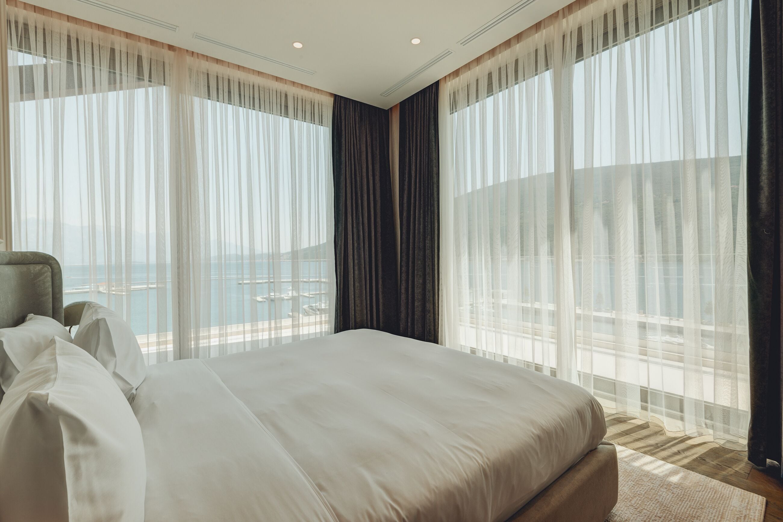 A hotel room with a large bed, a view of the sea, and sheer curtains.