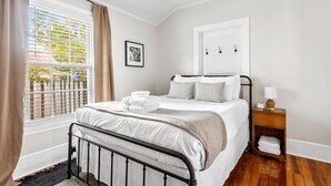 Ein ordentlich eingerichtetes Schlafzimmer mit Bett, Nachttisch und Lampe sowie einem Fenster mit Jalousien.