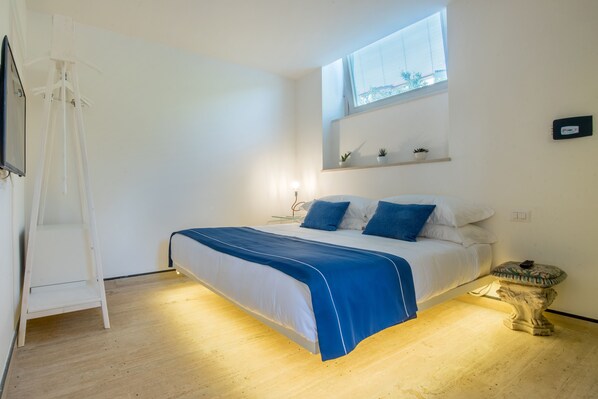A bedroom with a bed, a window, a shelf with plants, and a small table. - Da Rooms (Sorrento)