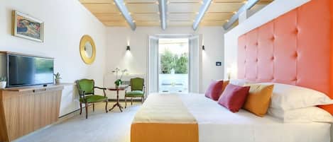 A modern hotel room with a large bed, a television, a dining area, and a view of the outdoors.