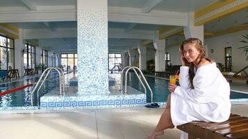 A pool area with a tiled mosaic column, wooden benches, and a person sitting by the pool.