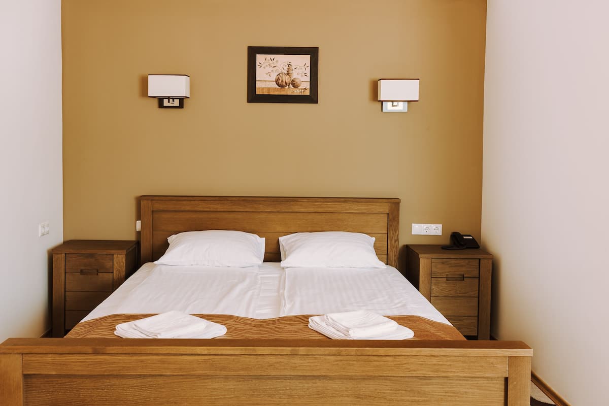 A neatly made bed with white linens, two bedside tables, a wall-mounted picture, and a phone on the nightstand.