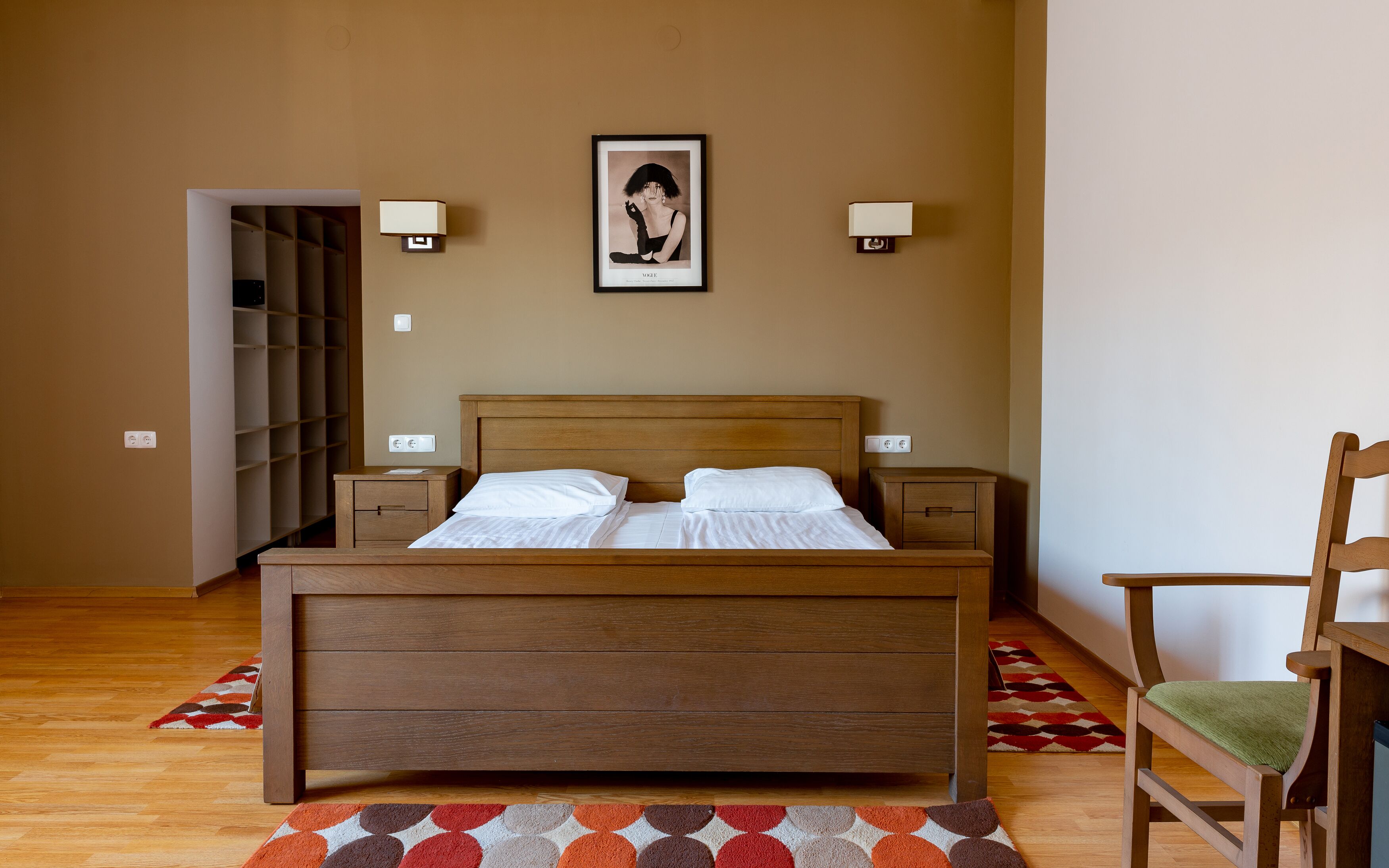 A bedroom with a wooden bed, two bedside tables, a chair, a wardrobe, and a framed picture on the wall.