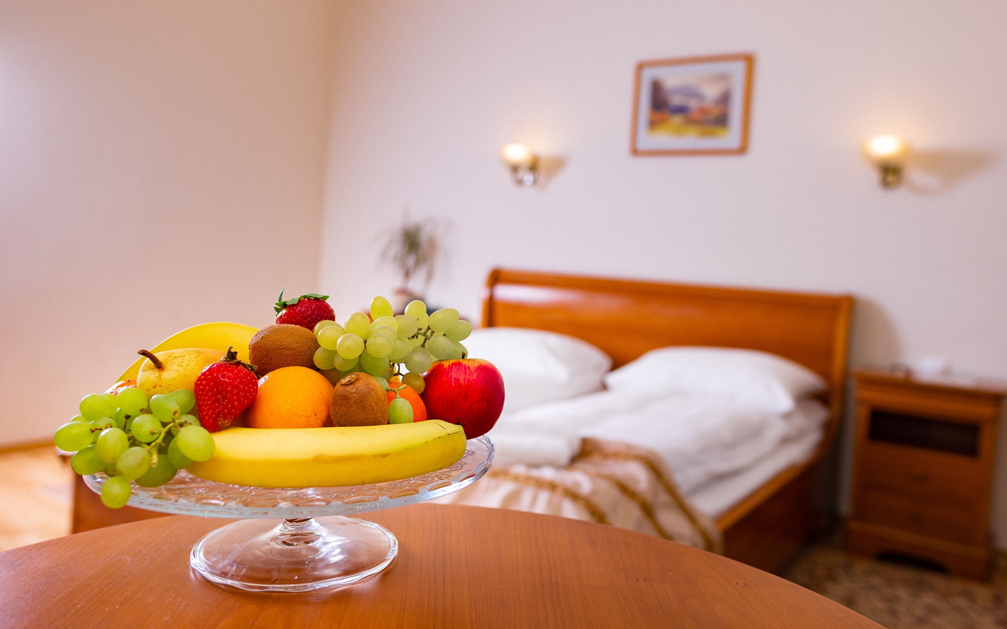 Een fruitschaal op een tafel in een hotelkamer, met een bed en nachtkastjes op de achtergrond.