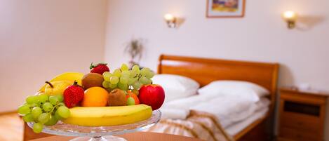 Een fruitschaal op een tafel in een hotelkamer, met een bed en nachtkastjes op de achtergrond.
