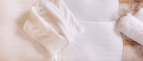 A neatly made bed with white linens and a folded towel on the pillow.