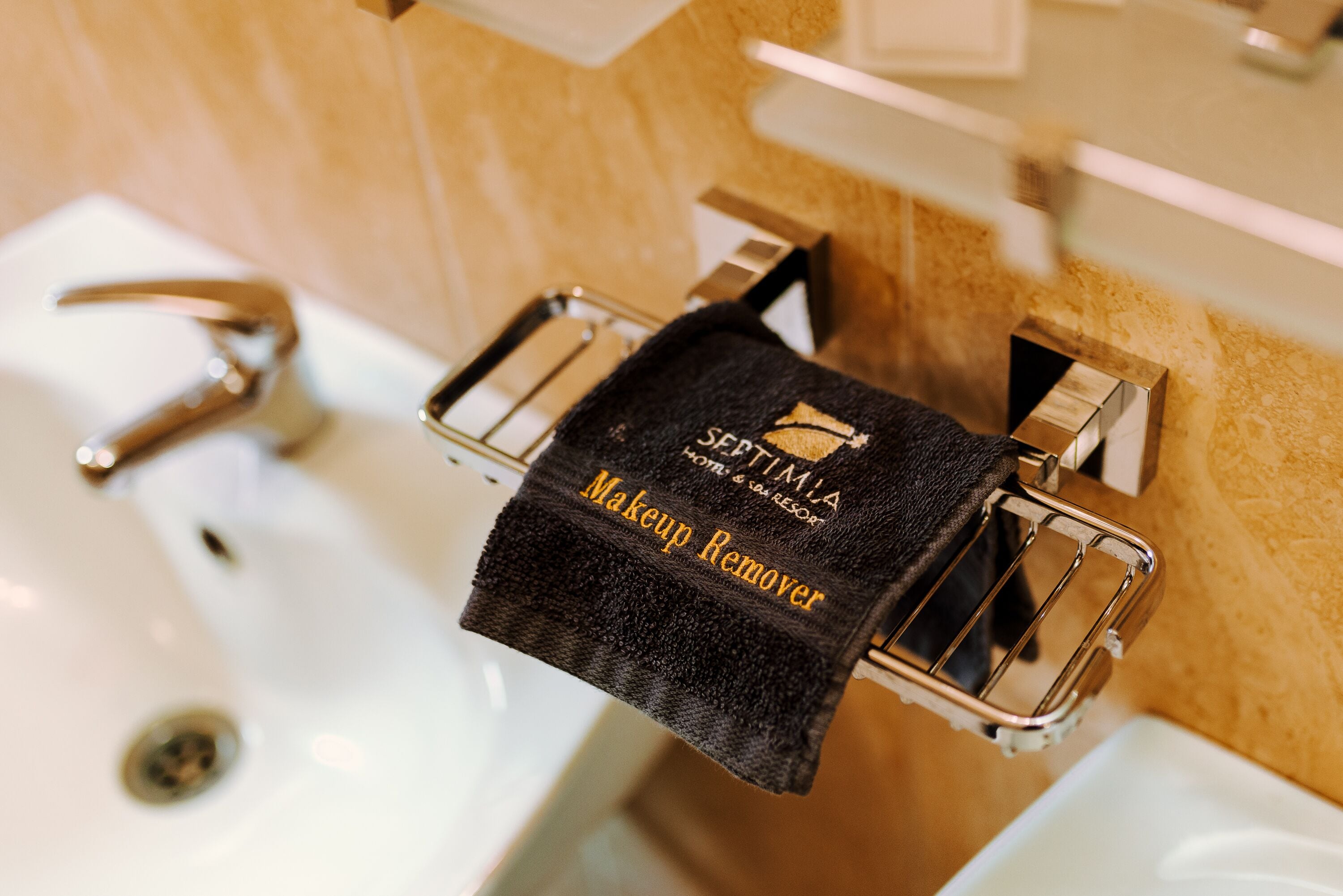A bathroom with a sink, mirror, and towel rack holding a black towel labeled "SEPTIMIA HOTEL & SPA RESORT Makeup Remover".