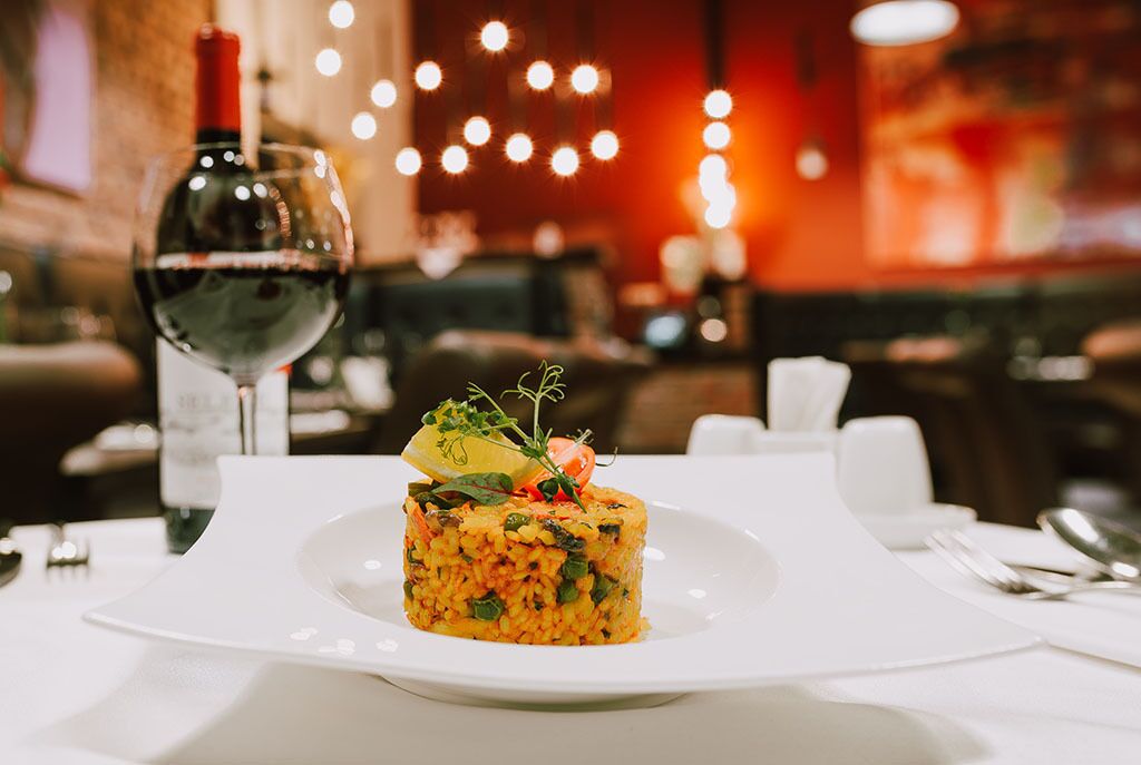 Una mesa de comedor con un plato de comida, una copa de vino tinto y una botella de vino.