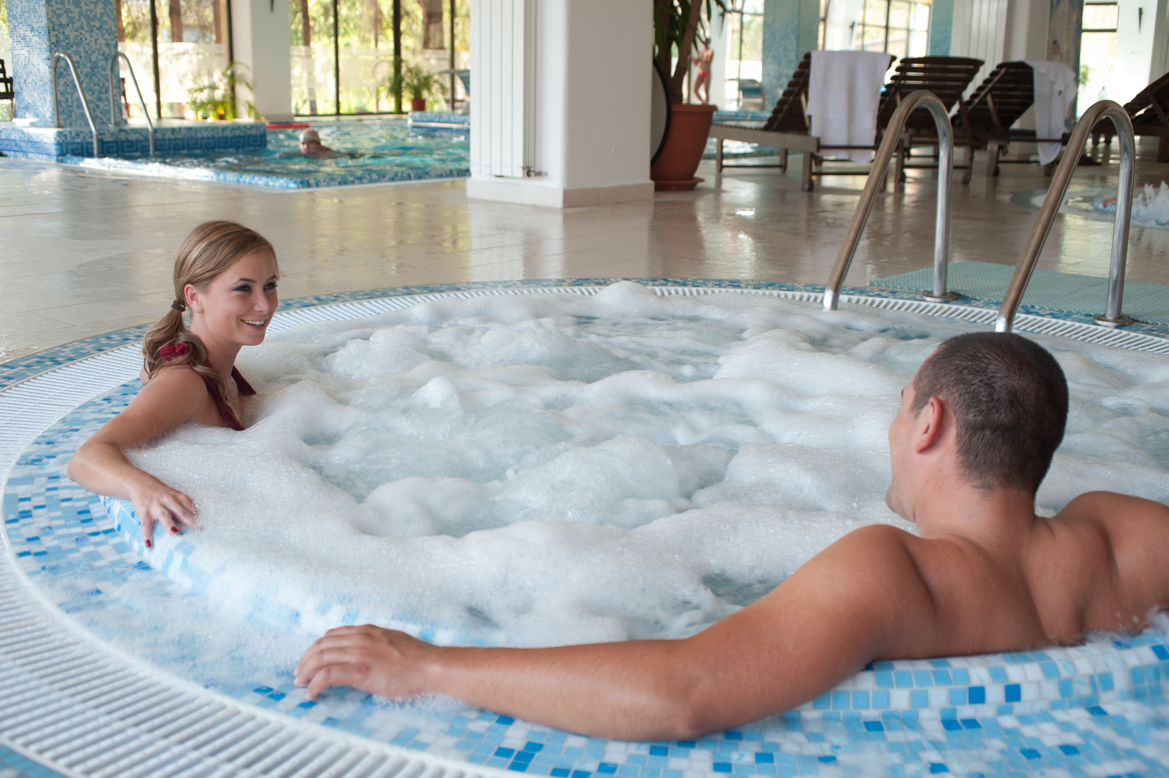 A hot tub with a tiled edge and a person sitting inside.