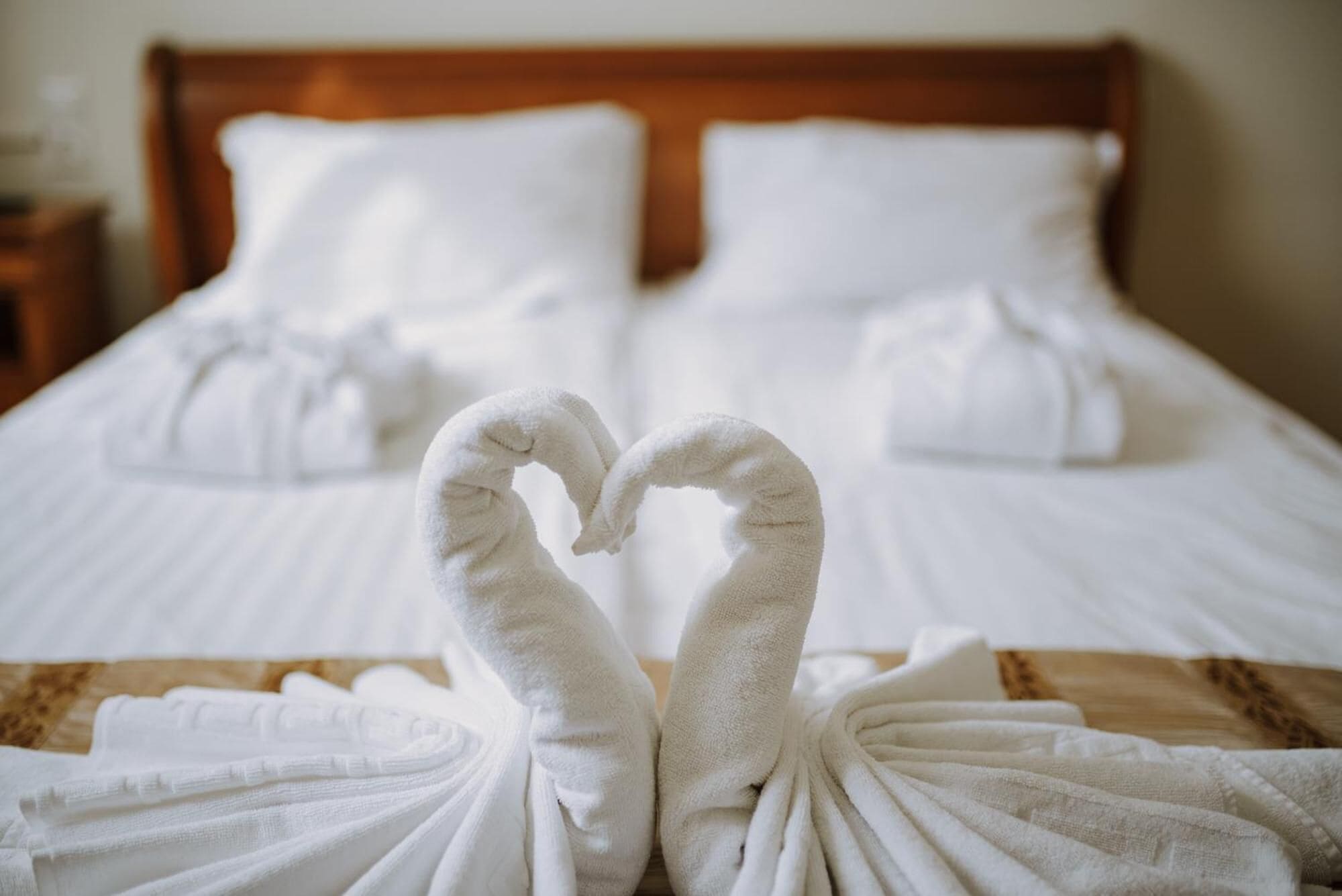 Una cama bien hecha con sábanas blancas y dos toallas dispuestas en forma de corazón.
