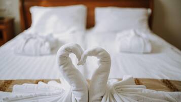 Una cama bien hecha con sábanas blancas y dos toallas dispuestas en forma de corazón.