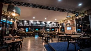 Un restaurante con zona de bar, mesas de madera y una pared de ladrillo decorada con varios carteles.