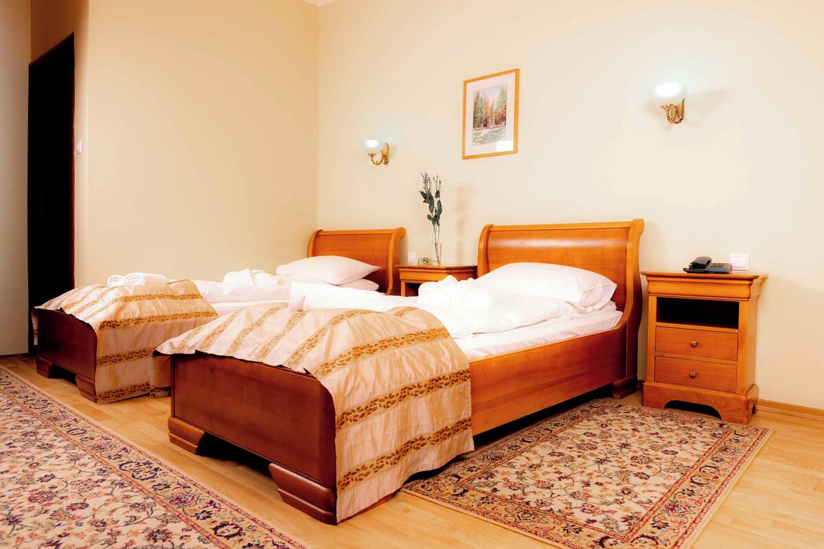 A hotel room with two wooden beds, a nightstand with a phone, a wall-mounted light, and a framed picture.