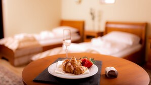Habitación de hotel con una mesa redonda dispuesta para el desayuno, que incluye croissants, fresas y una copa de vino.