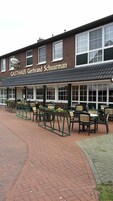 A brick building with a sign reading "GASTHAUS Gerbrand Schuurman" and outdoor seating with tables and chairs.
