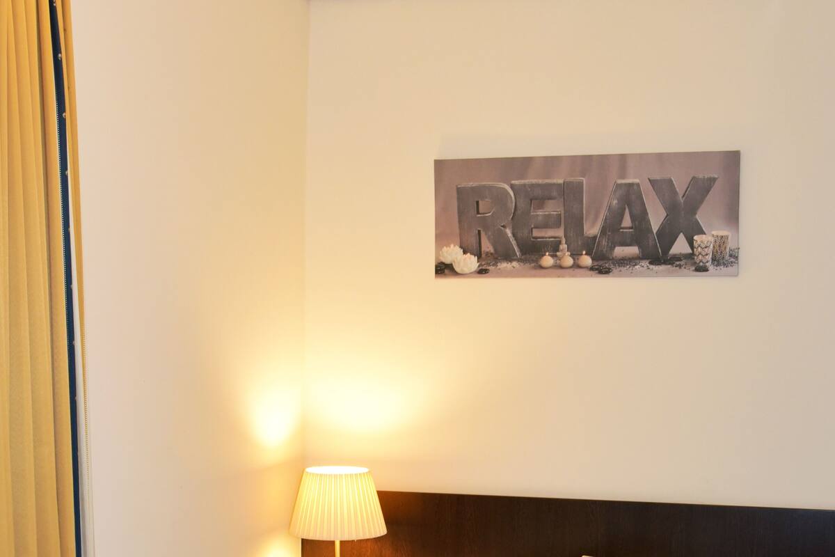 A neatly made bed in a hotel room with a wall-mounted sign that reads "RELAX".
