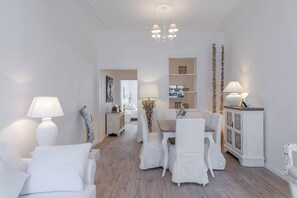 A dining area with white furniture, a chandelier, and a cabinet with decorative items.