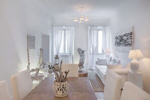 A modern living room with a dining table, white sofas, and a chandelier.