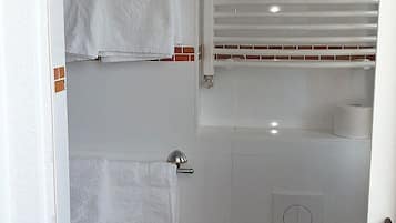 Ein kleines, abgeschlossenes Badezimmer mit Toilette, Handtuchhalter und einem Fenster mit Jalousien.