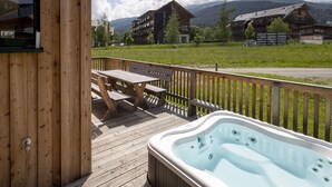 A wooden deck with a hot tub and picnic table, overlooking a mountain landscape.