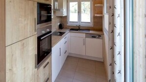 A compact kitchen with wooden cabinets, a built-in oven, a microwave, and a window above the sink.