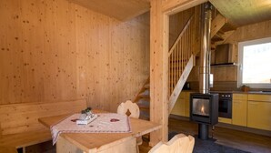 Een houten interieur met een eettafel, stoelen, een trap en een keukenhoek.