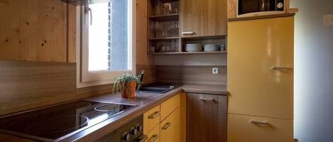 A compact kitchen with wooden cabinets, a built-in oven, a microwave, and a refrigerator.