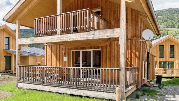 Een houten chalet met balkon, een schotelantenne en uitzicht op het omliggende landschap.