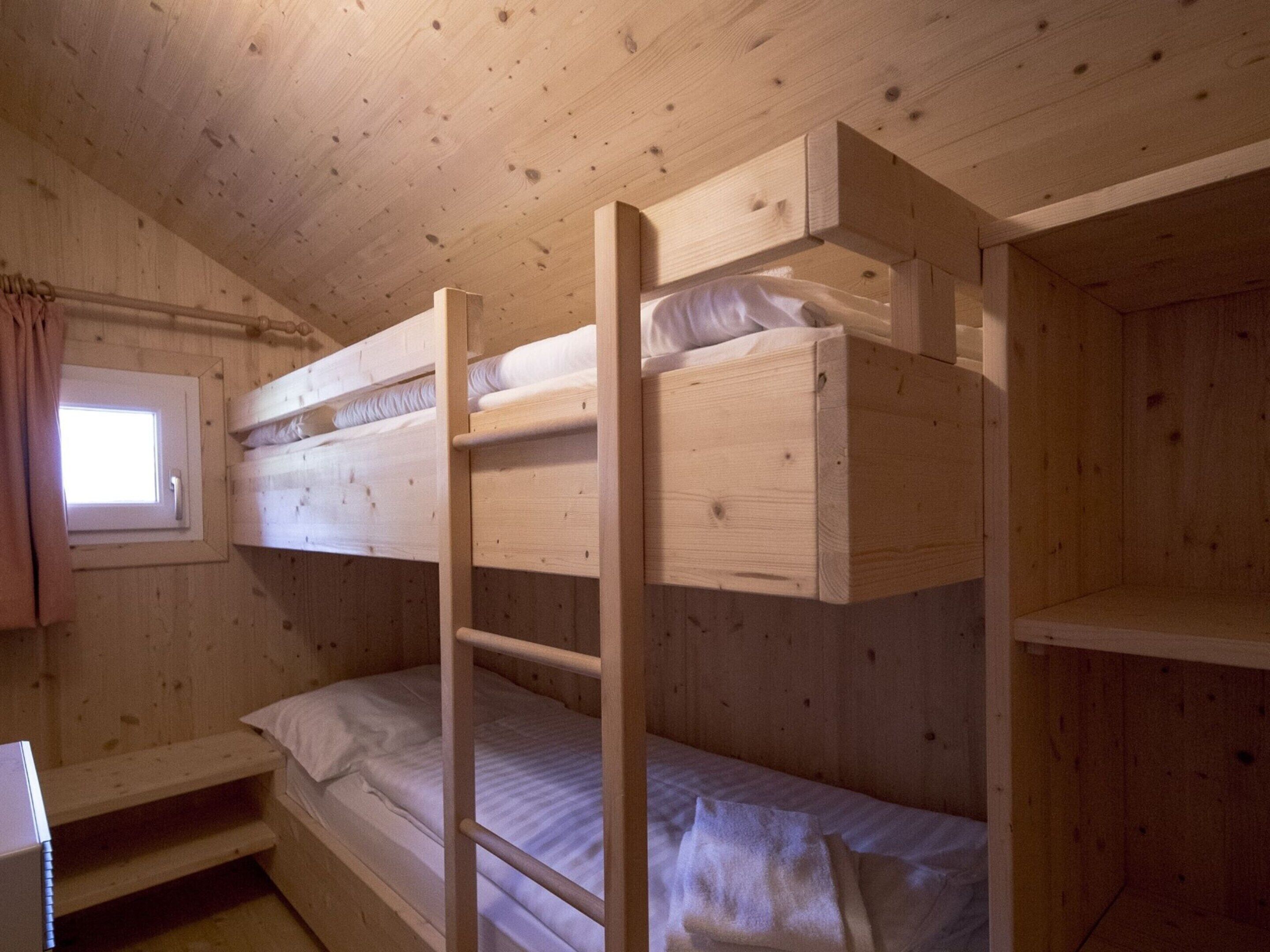 Une chambre avec un lit superposé, des murs en bois et une fenêtre.