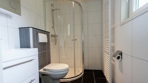 A modern bathroom with a glass-enclosed shower, a toilet, and a white sink. - Chalet Near Campground (De Bult)
